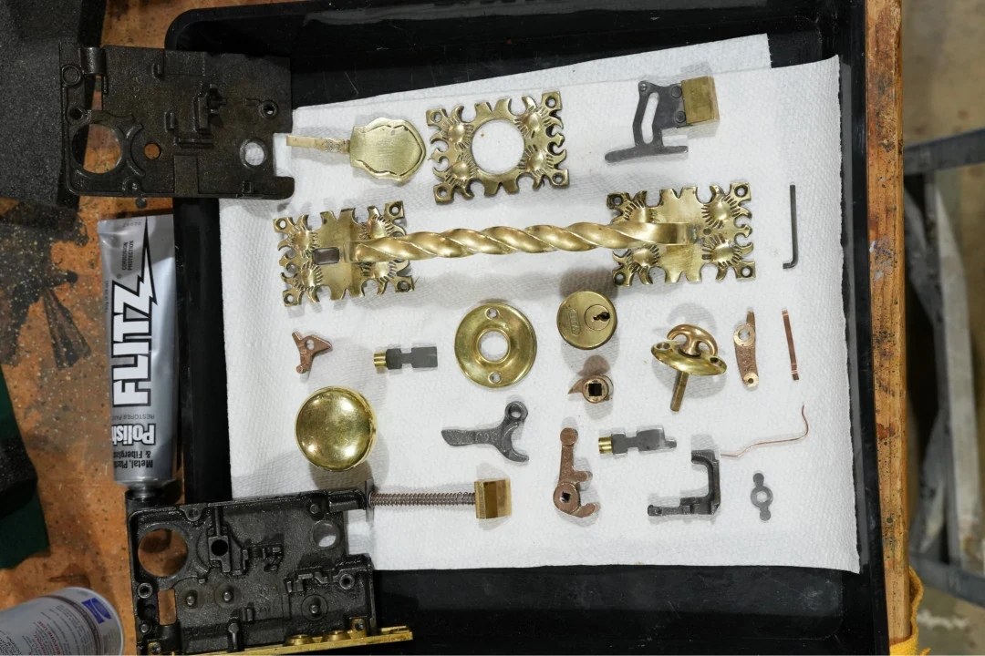 Polished brass handles, ornamental plates, Yale cylinder, and antique mortise lock parts on a workshop tray