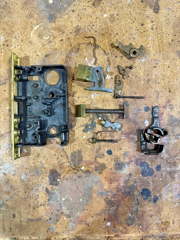 Antique mortise lock case, springs, levers, and brass bolts fully disassembled on a workbench