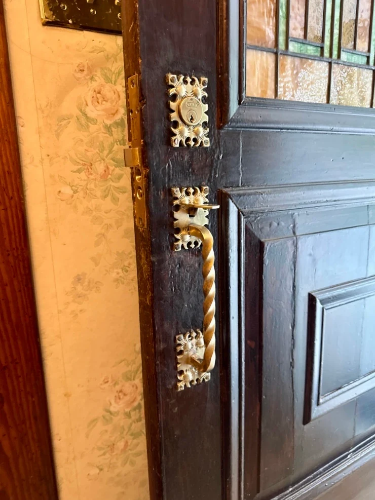 Restored rope-pattern brass thumb-latch handle and Yale cylinder on the Victorian stained-glass door