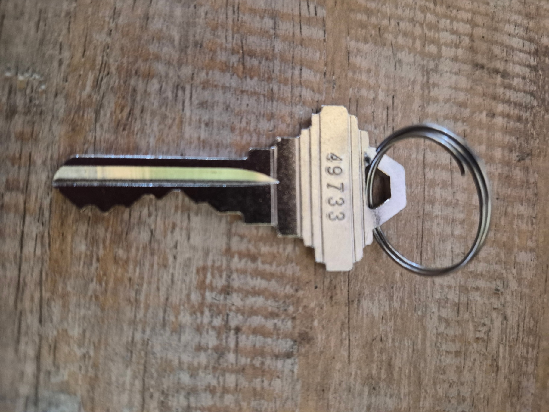 Close-up of an intact metal building key with a black-and-light-colored integrated head and circular key ring on a wood-like surface