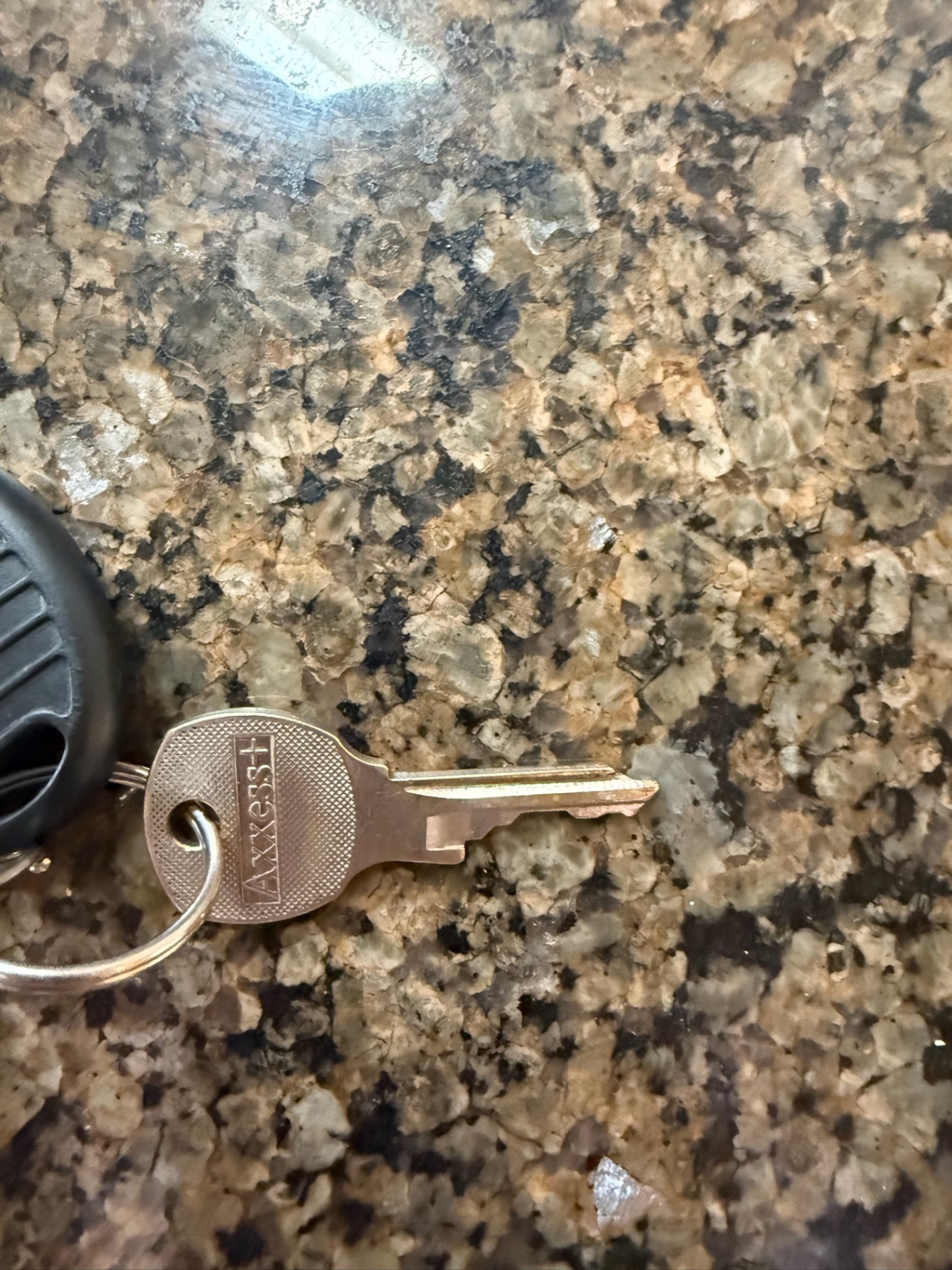Close-up of an intact metal mailbox key with stamped lettering attached to a circular key ring on a mottled countertop.