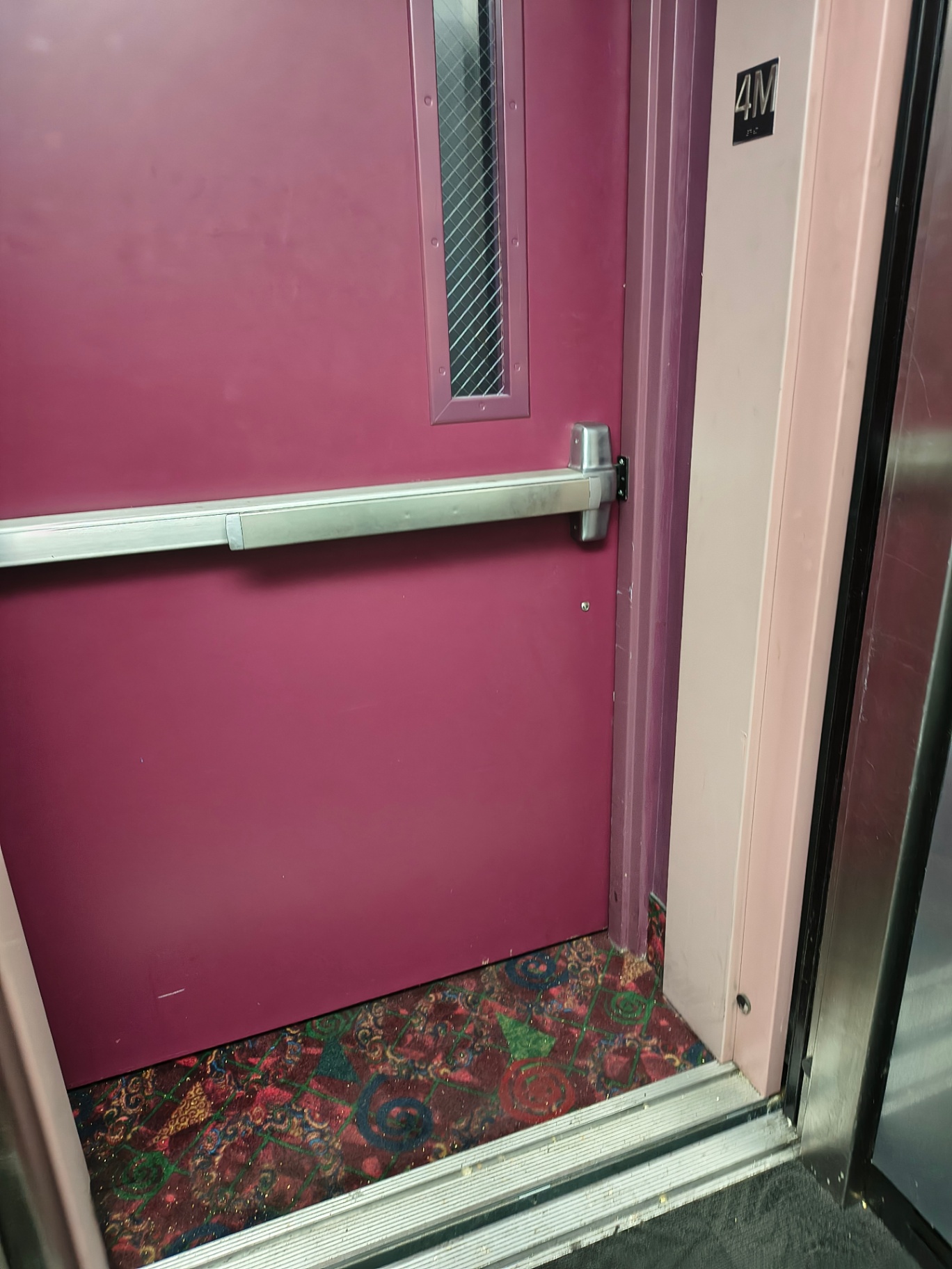 Burgundy commercial exit door in a Denver facility with a narrow wired-glass vision panel, panic bar, and brushed-metal lock escutcheon - view 7