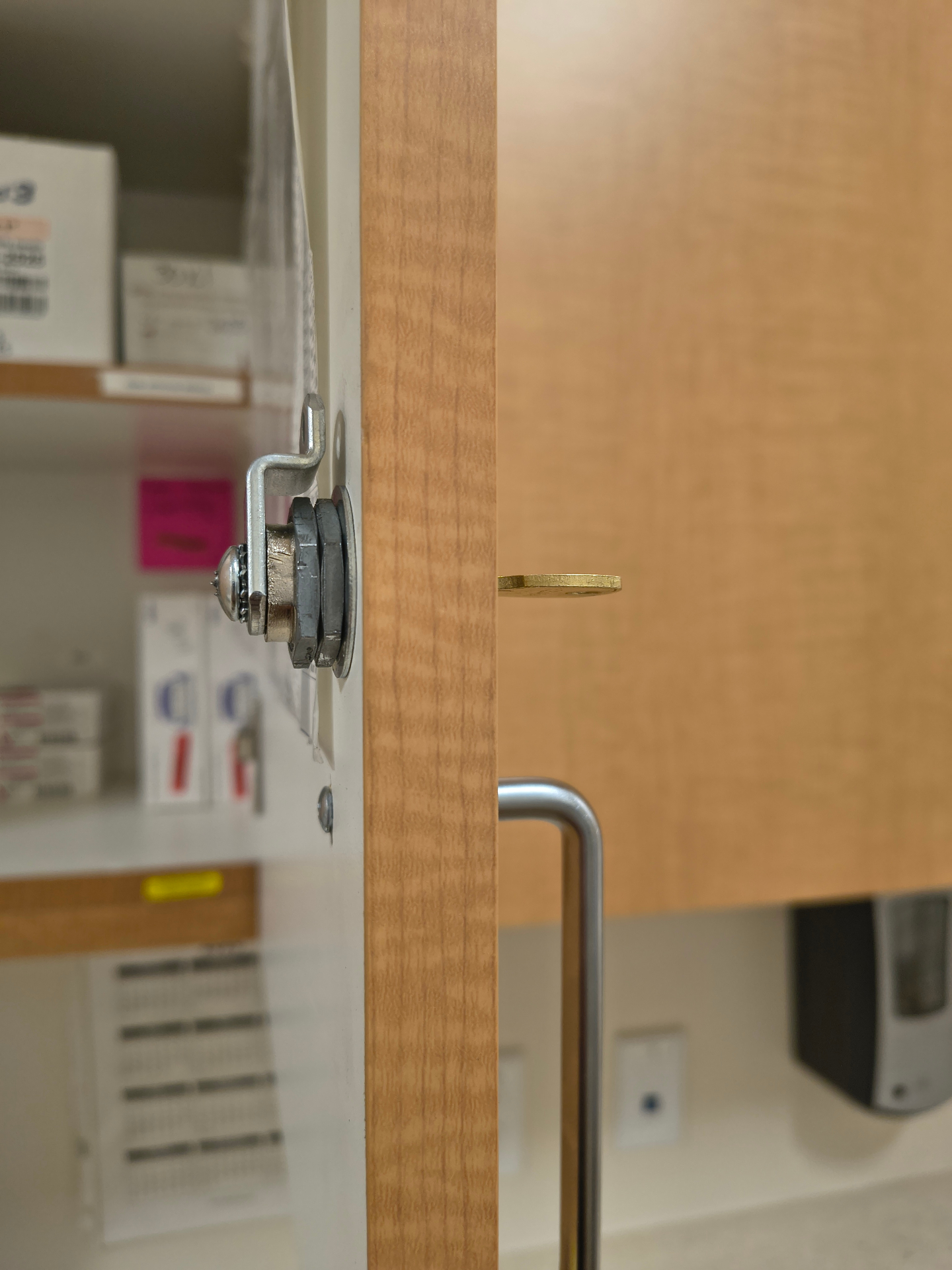 Exposed cylindrical cam lock with brass-colored key on a wood-finish interior cupboard beside an electronic access device in Westminster - view 3