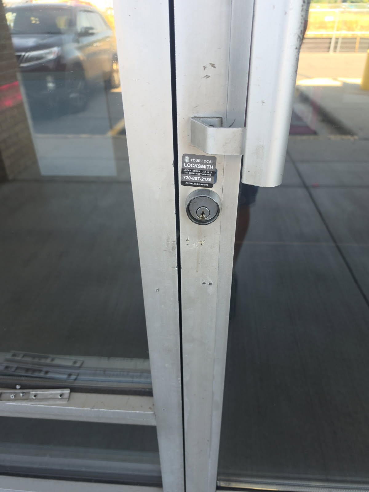 Close-up of a worn keyed cylindrical lock and pull handle on an aluminum-framed glass storefront door in Denver. - view 6