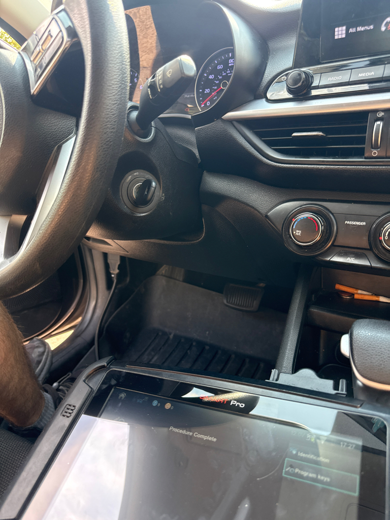 Locksmith holds a black automotive key fob beside a gray passenger vehicle on a Denver street; interior view shows a key in the ignition and a diagnostic tablet displaying a comple - view 2