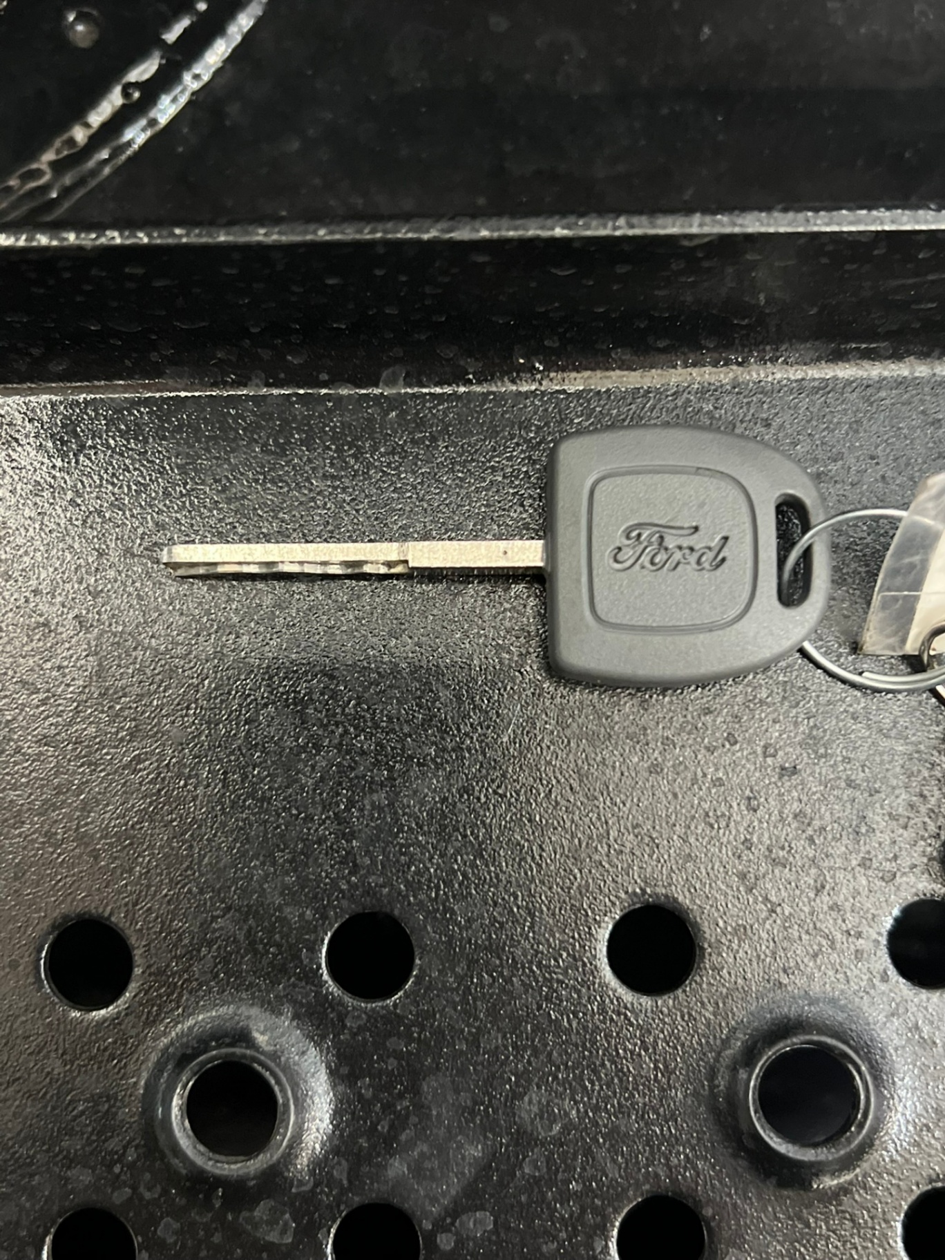 Close-up of a black vehicle remote key fob with lock, unlock, and panic buttons beside a Ford-branded mechanical key with visible blade cuts. - view 3