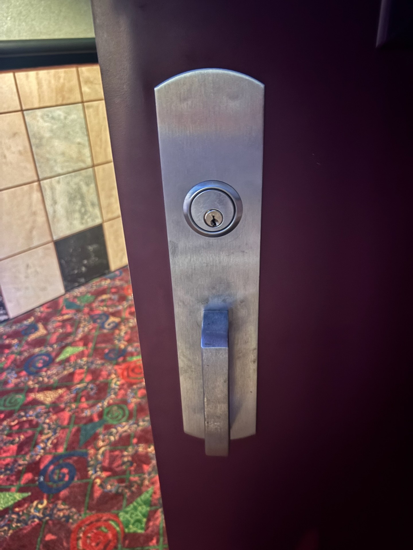 Burgundy commercial exit door in a Denver facility with a narrow wired-glass vision panel, panic bar, and brushed-metal lock escutcheon