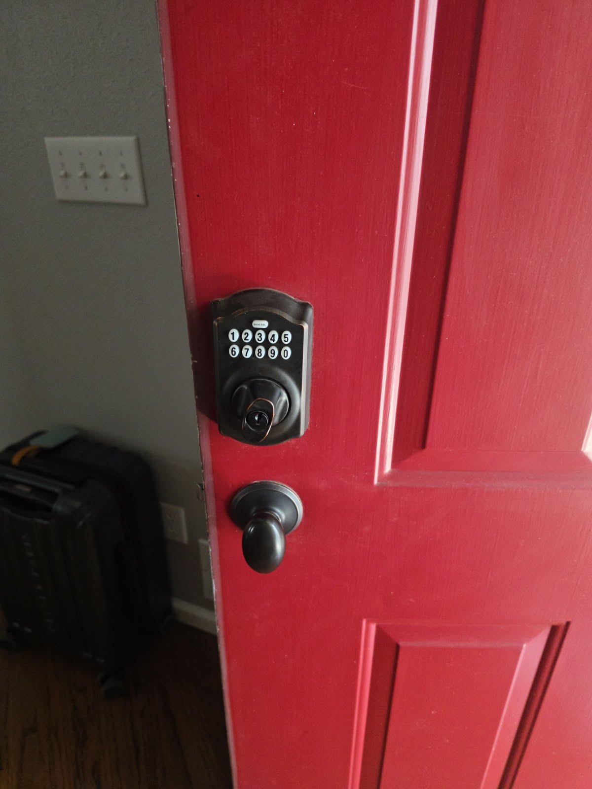 Black electronic keypad deadbolt above a separate round knob on a white paneled residential entry door - view 2
