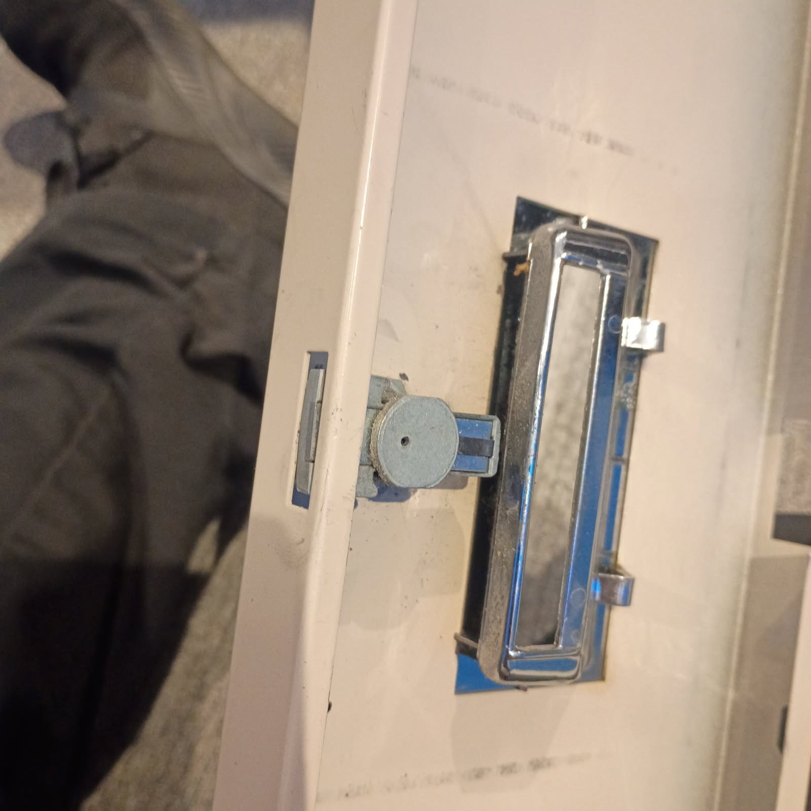 Close-up of a worn commercial cabinet or door with a chrome pull handle, round keyed cylinder, and exposed latch mechanism.
