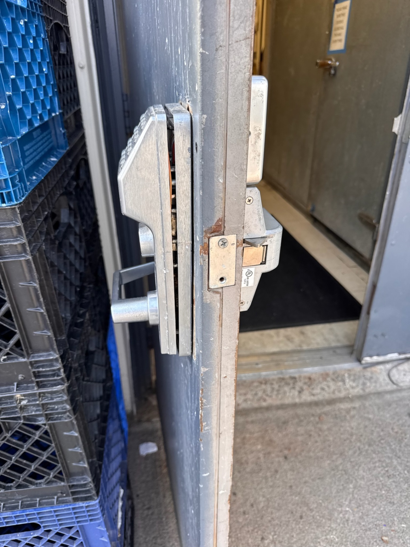 Commercial metal door with a silver numeric keypad lock, key cylinder, lever handle, rust, and exposed mounting holes. - view 2