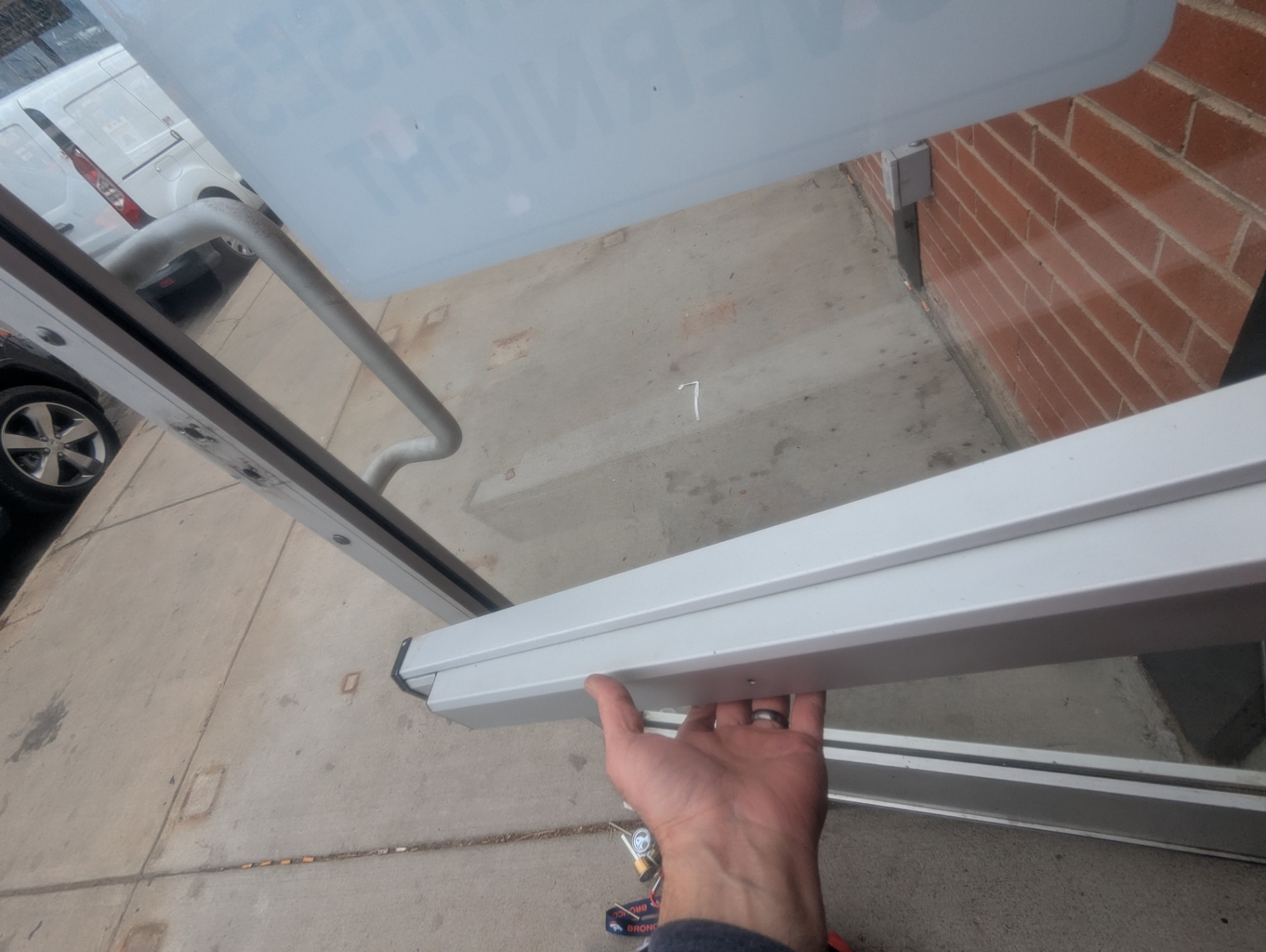 Locksmith handling a rim-cylinder component and keys at a Denver commercial glass storefront entrance with panic-bar hardware visible nearby. - view 4
