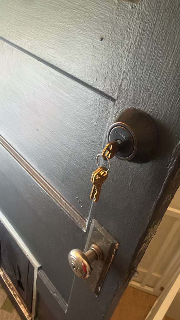Residential locksmith case study showing a white barred security door with cylindrical deadbolt and knob, an older wood-door lockset, and a dark painted door with keys in its deadb - view 3
