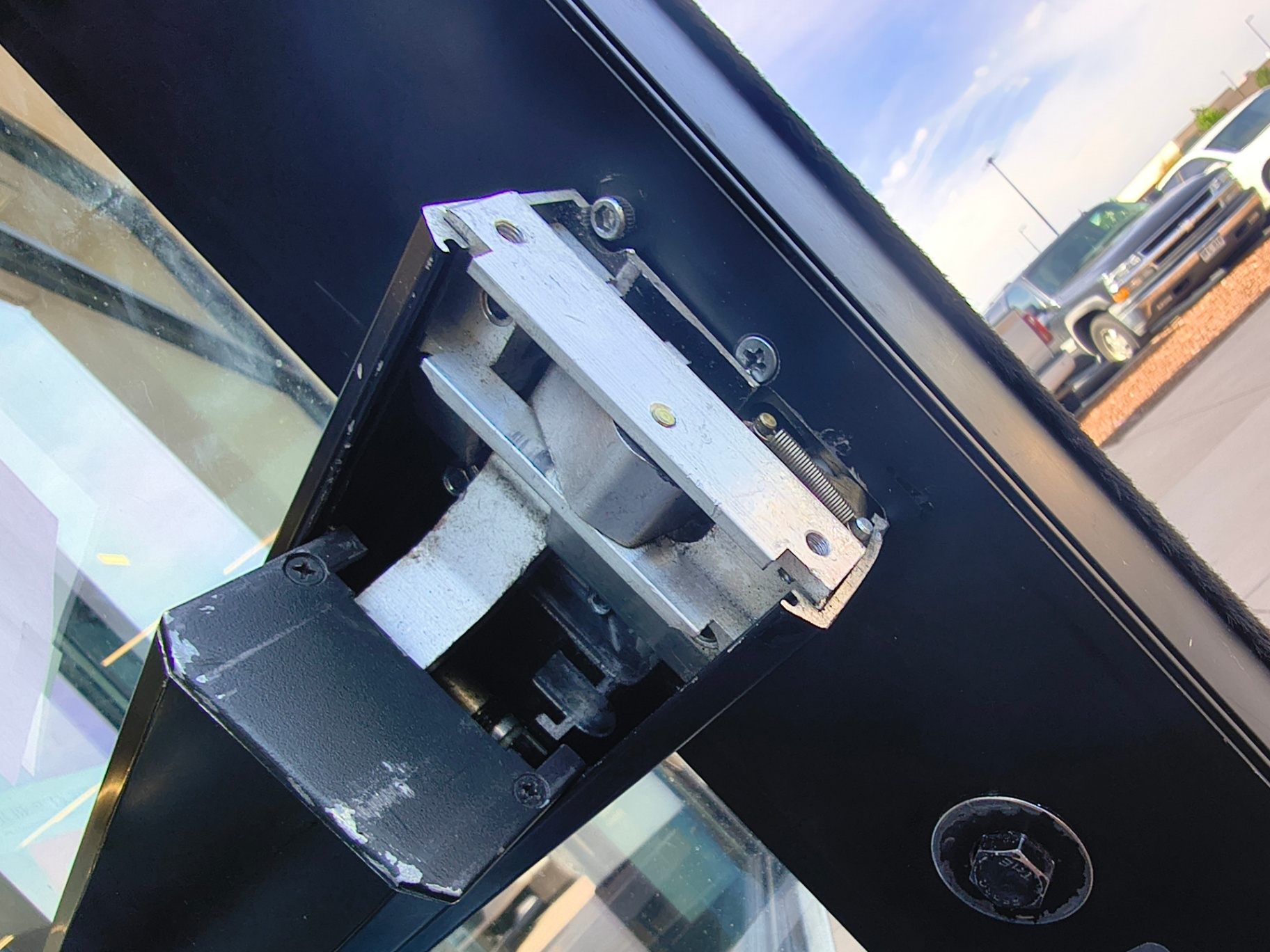 Gloved hand holding worn commercial exit-device hardware removed from a black-framed glass entrance in Westminster - view 2