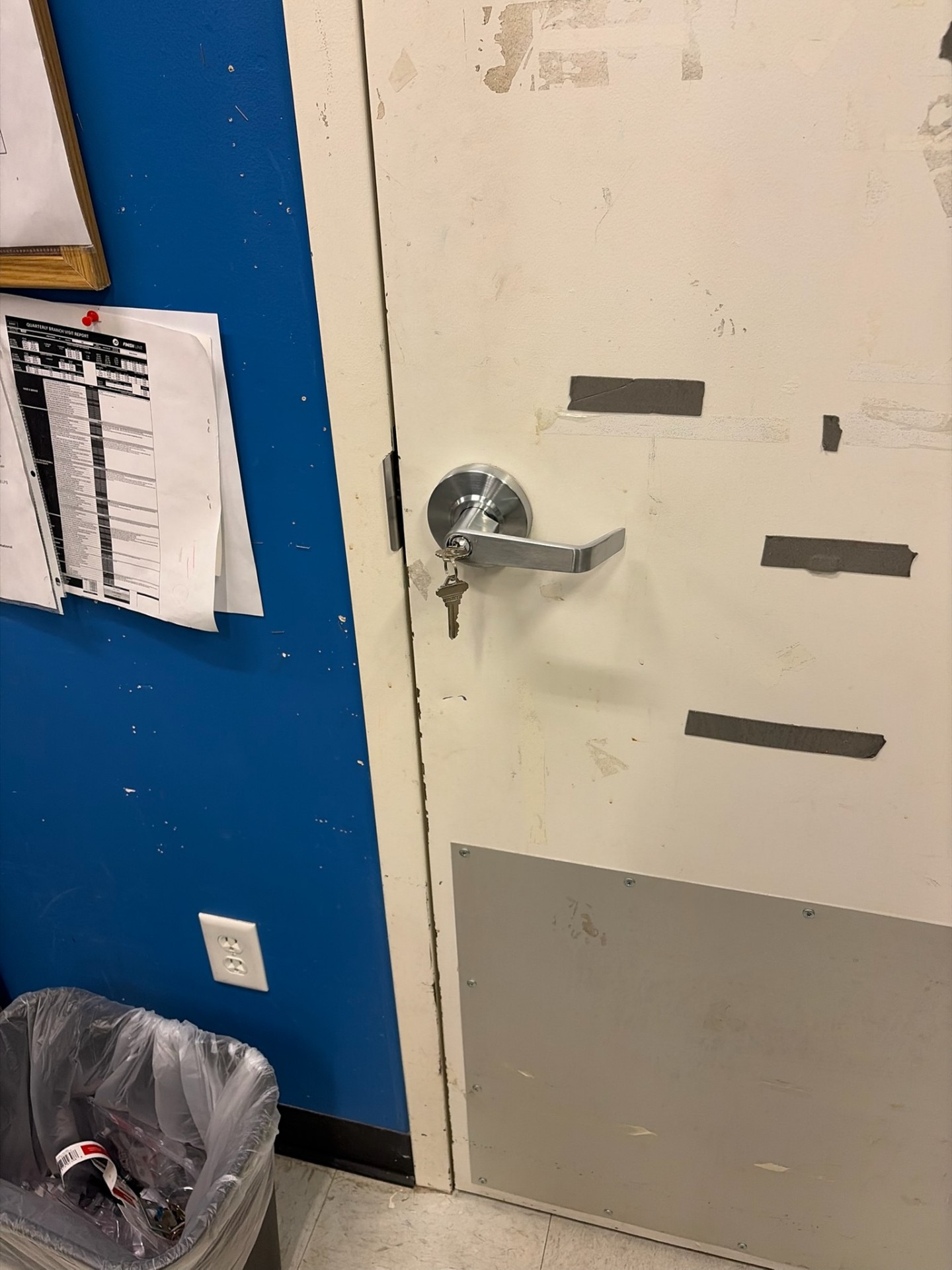 Commercial restroom door in Westminster with a metal keyed lever, keys at the cylinder, exposed latch, worn paint, and lower protective plate. - view 2