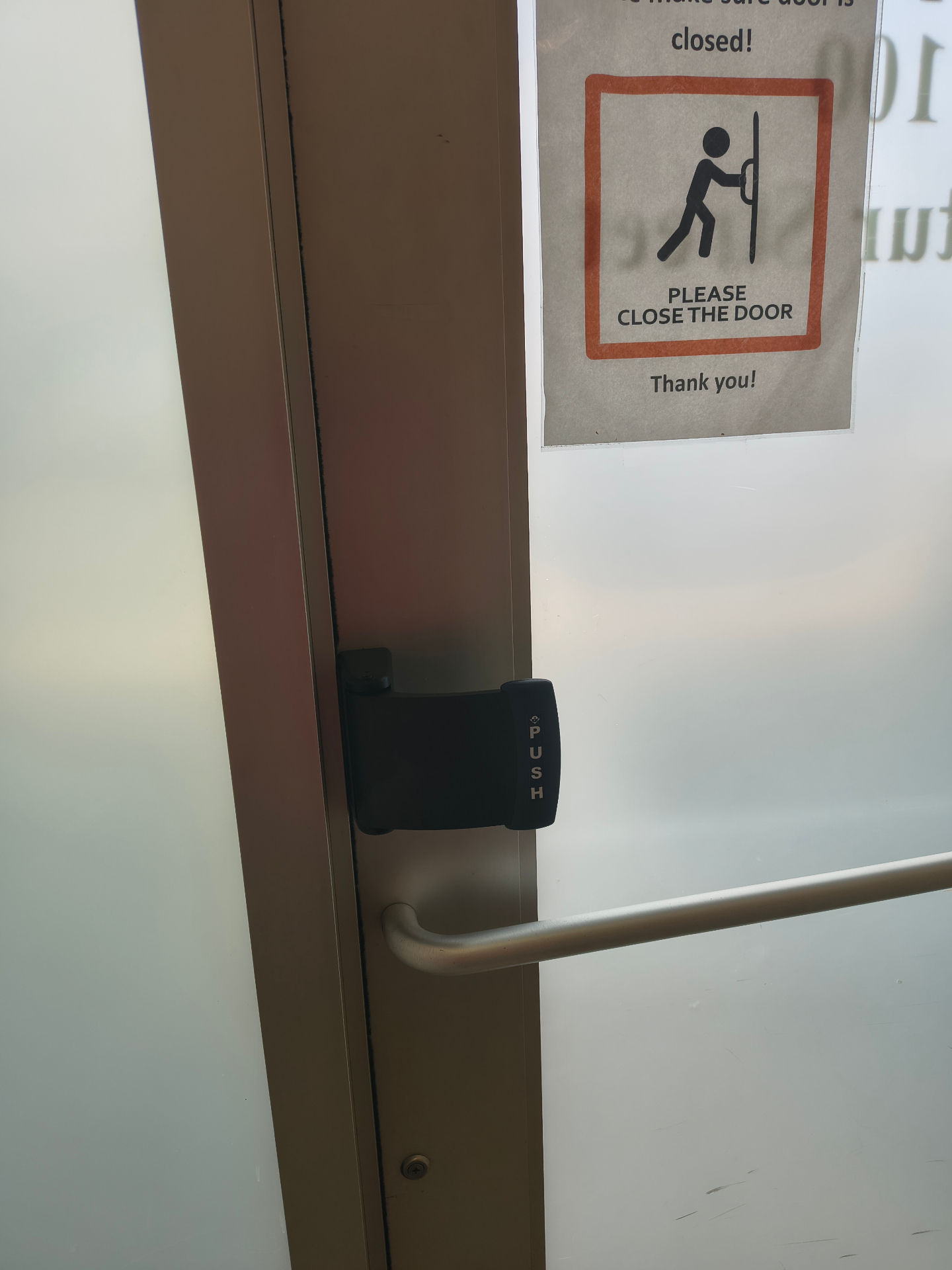 Open glass-and-aluminum commercial door showing exposed mortise lock hardware, pull handle, and black push exit device - view 3