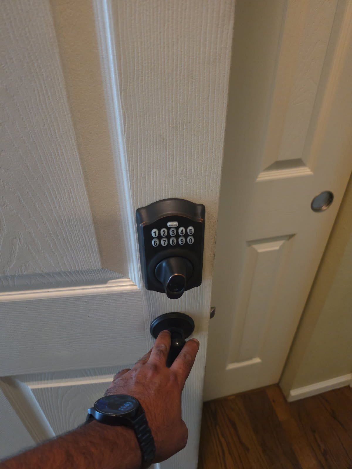 Black electronic keypad deadbolt above a separate round knob on a white paneled residential entry door