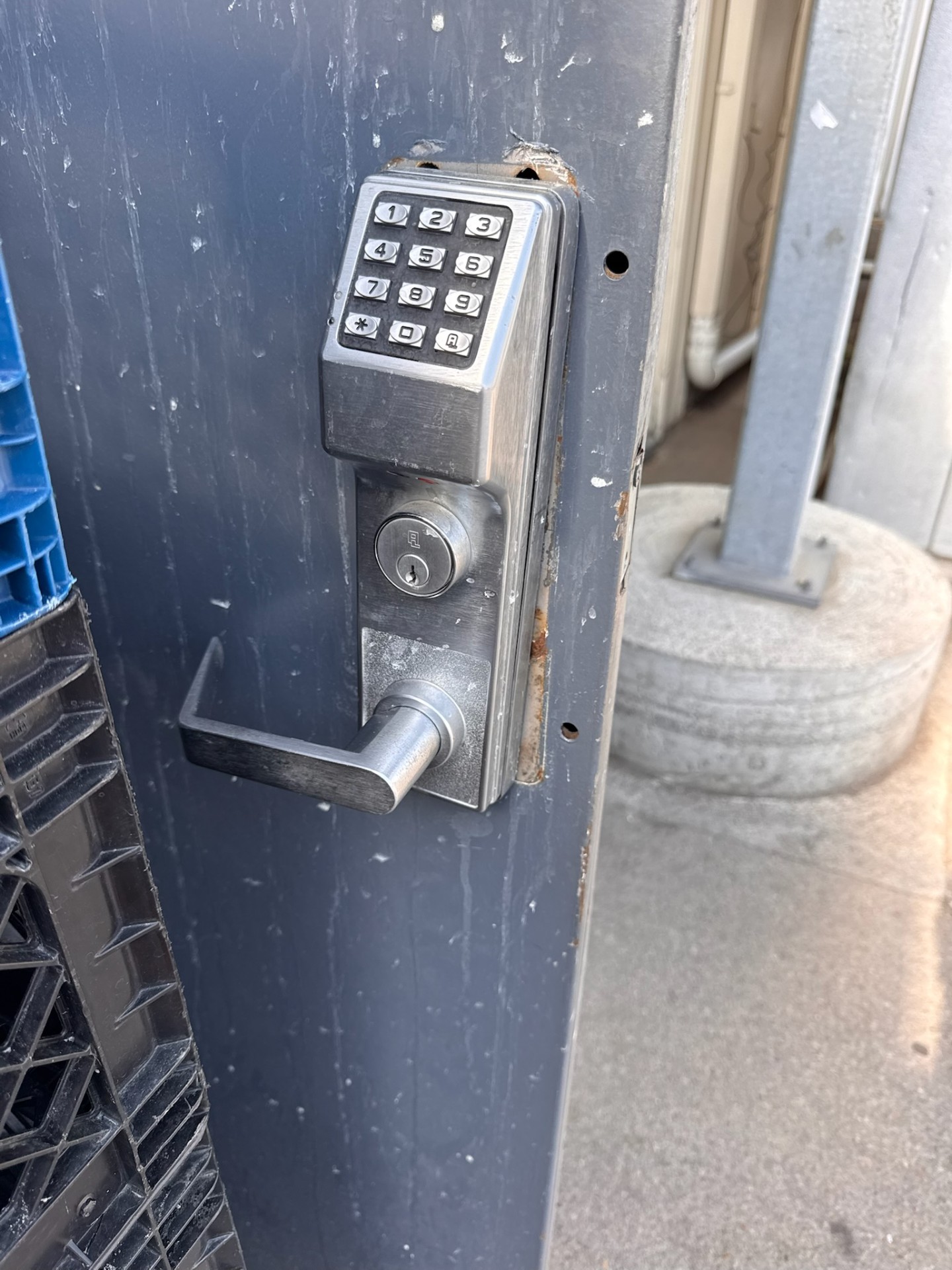 Commercial metal door with a silver numeric keypad lock, key cylinder, lever handle, rust, and exposed mounting holes. - view 3