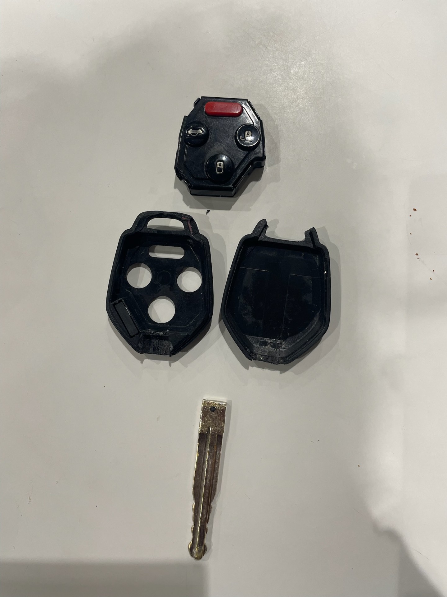 Disassembled black multi-button car key fob shell, internal fob component, and used metal key blade on a plain surface