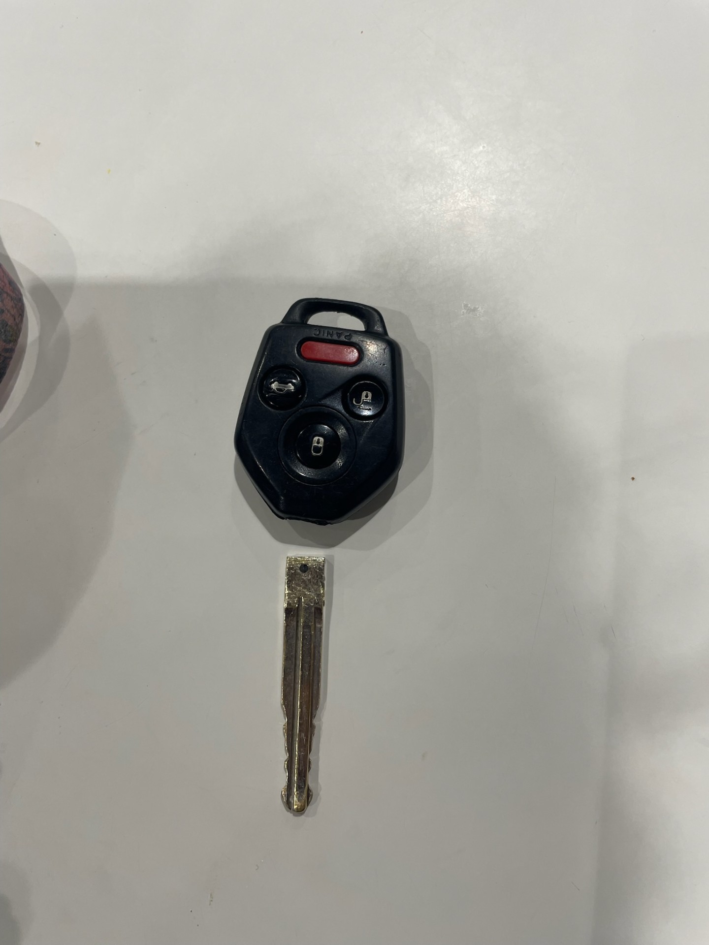Disassembled black multi-button car key fob shell, internal fob component, and used metal key blade on a plain surface - view 2