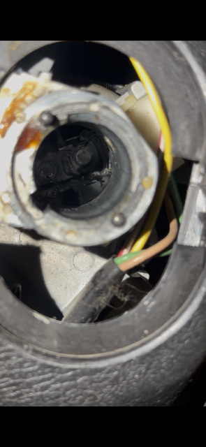 Close-up of an exposed circular vehicle lock assembly with a dark central component, colored wiring, and removed surrounding trim.