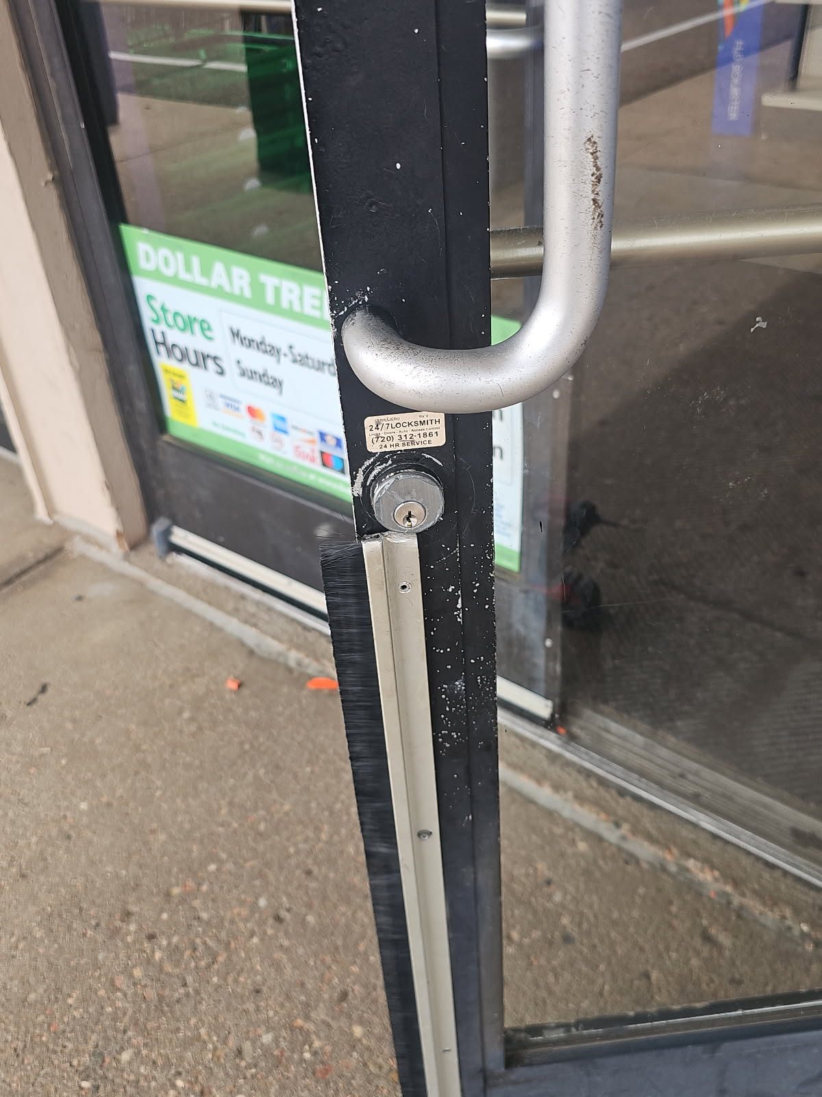 Close-up of a keyed cylinder below a large vertical pull handle on a worn black-framed glass storefront door in Lakewood, Colorado - view 2