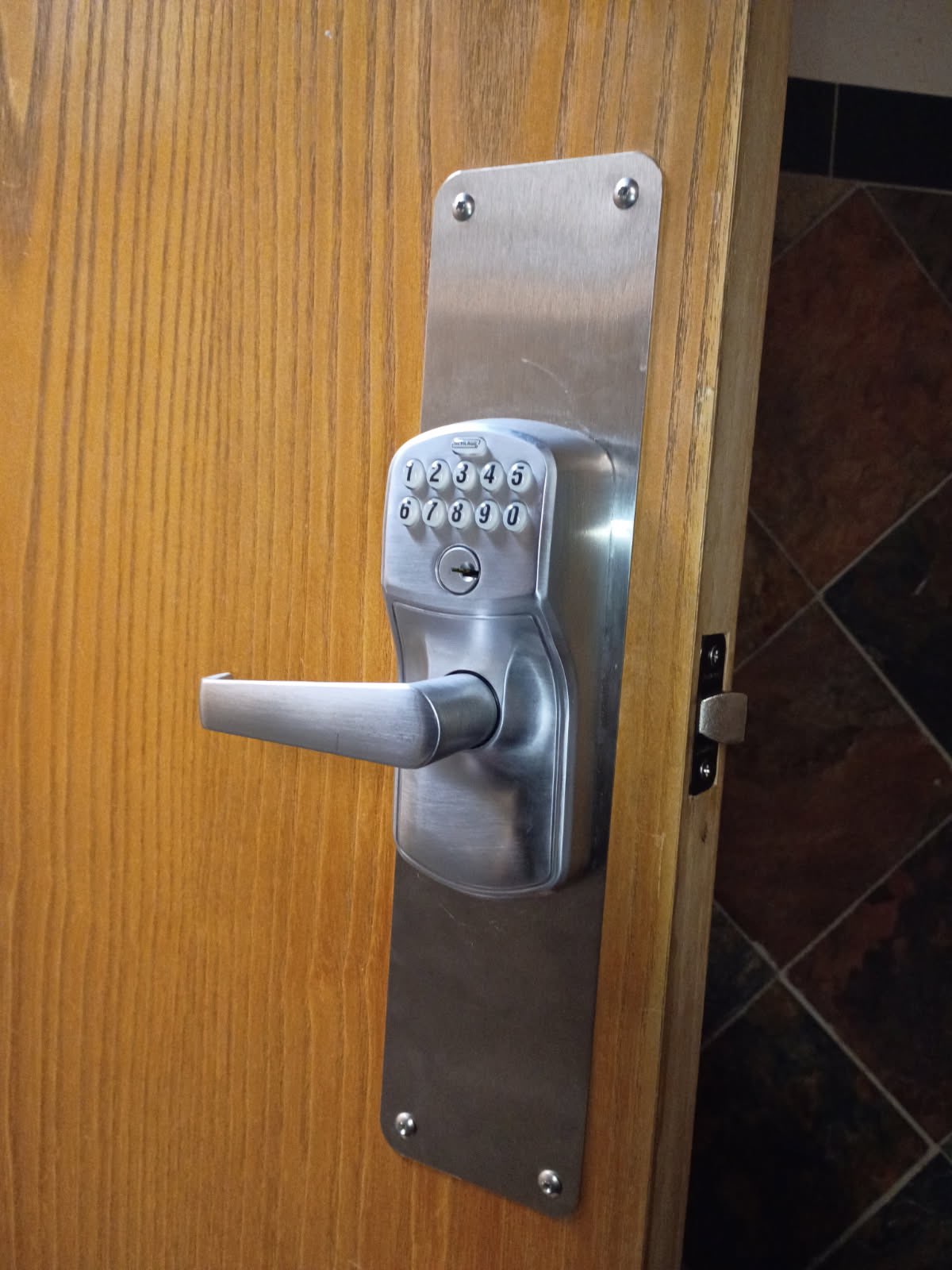 Silver keypad lock with lever handle and metal backplate installed on a partially open wood-finish interior door