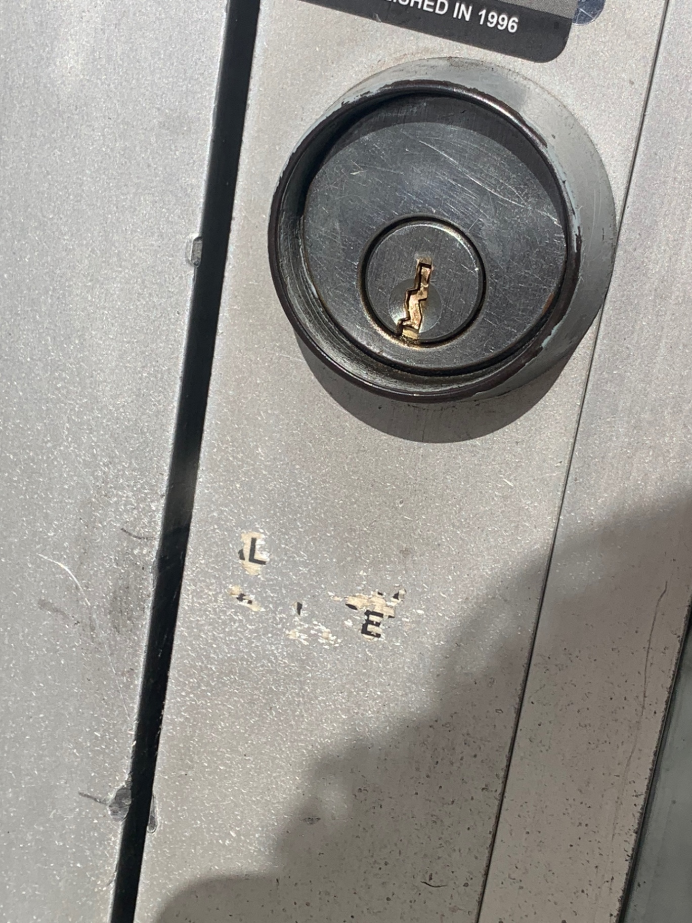 Close-up of a worn keyed cylindrical lock and pull handle on an aluminum-framed glass storefront door in Denver. - view 3