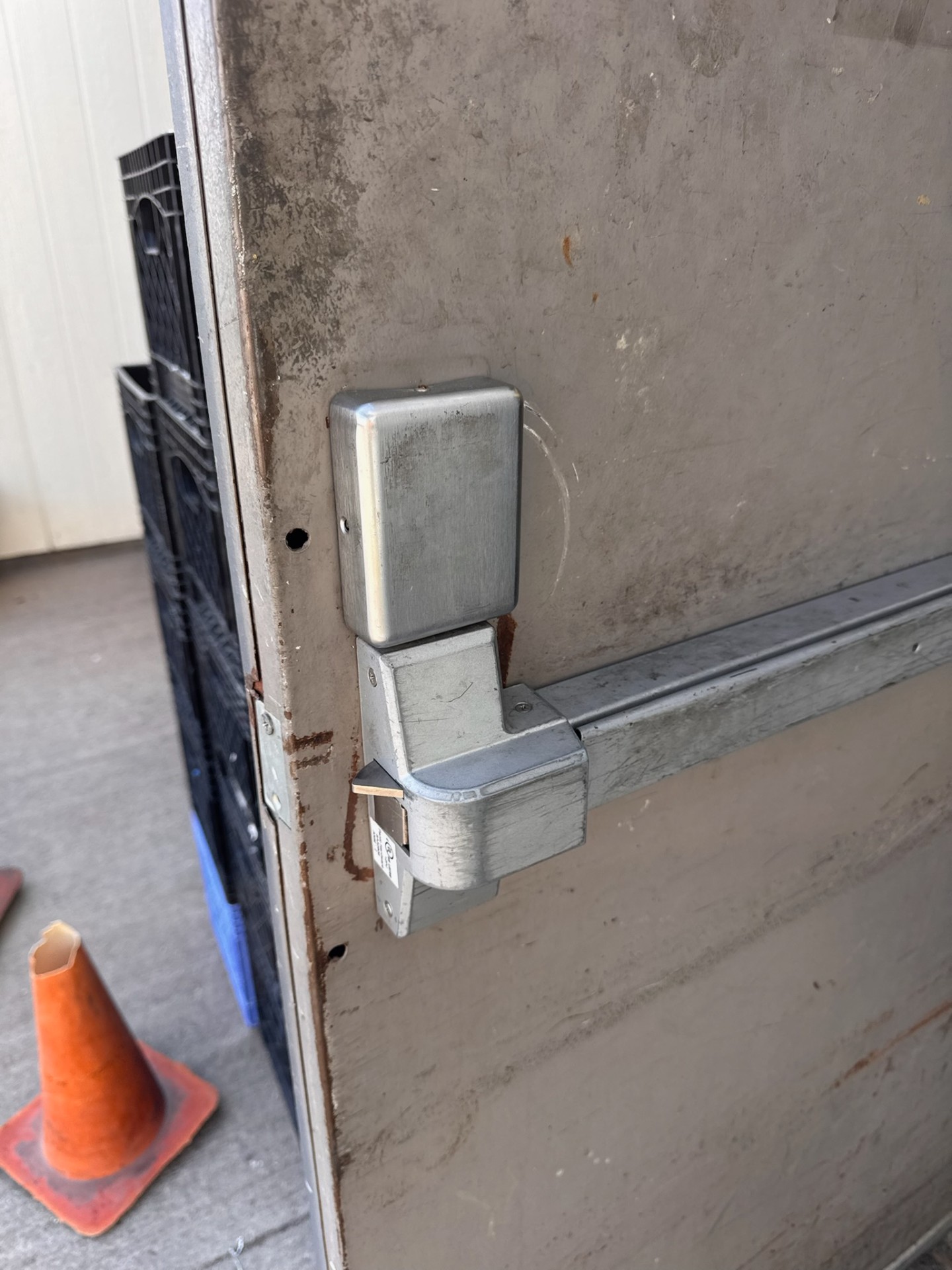 Commercial metal door with a silver numeric keypad lock, key cylinder, lever handle, rust, and exposed mounting holes.