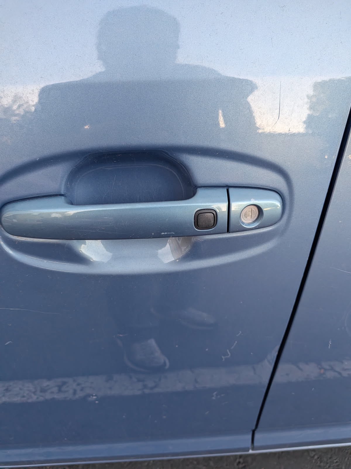 Close-up of a blue-gray vehicle driver’s door with an exterior handle, push button, and mechanical key lock cylinder
