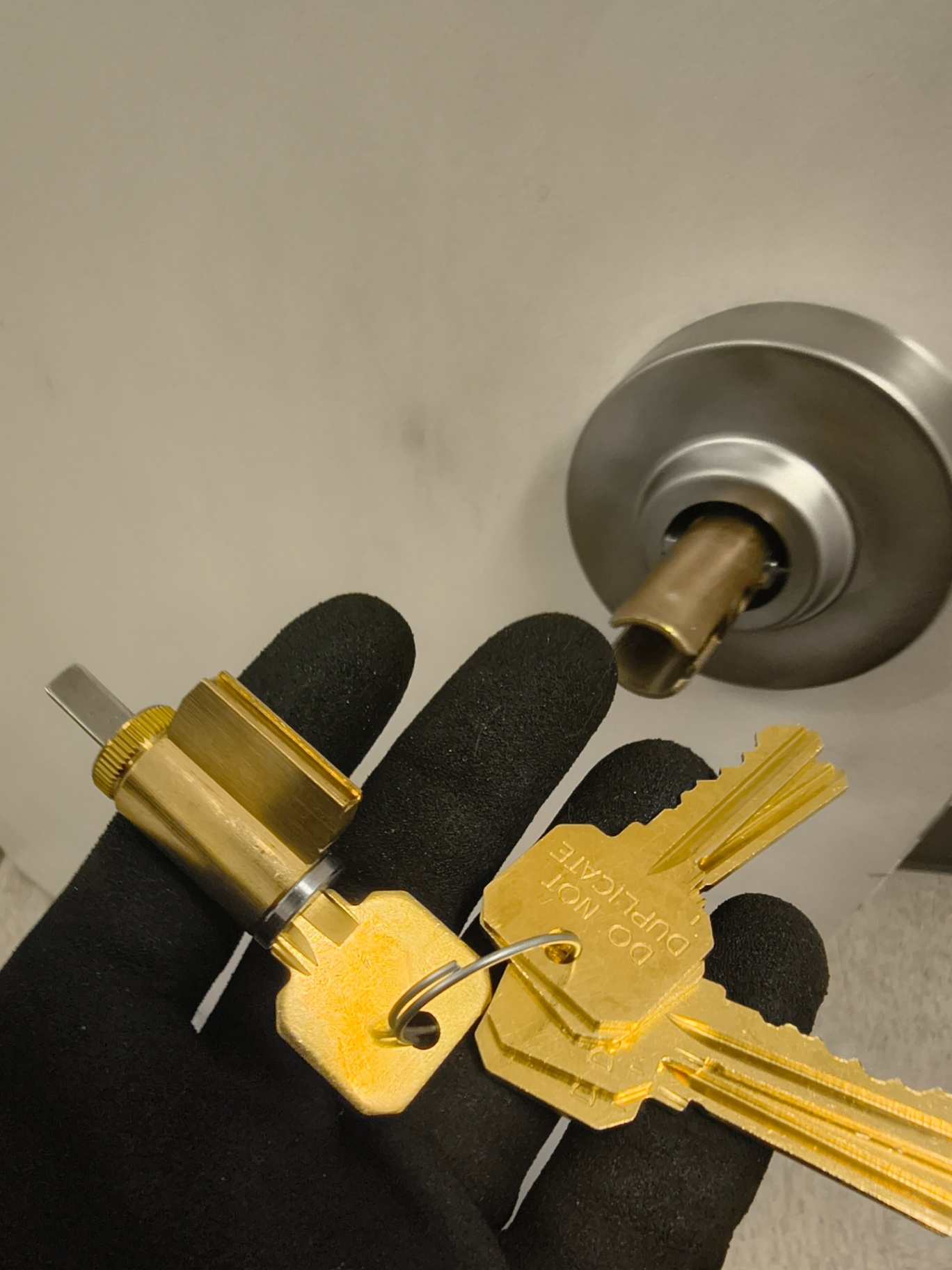 Gloved locksmith holding a gold-colored cylinder and keys beside a silver commercial restroom door knob