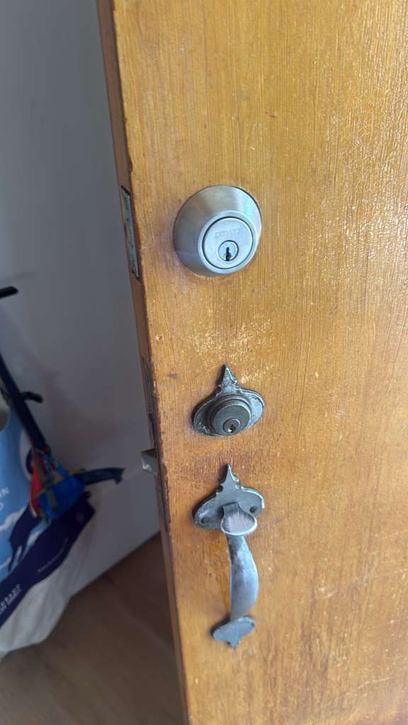 Residential locksmith case study showing a white barred security door with cylindrical deadbolt and knob, an older wood-door lockset, and a dark painted door with keys in its deadb - view 2
