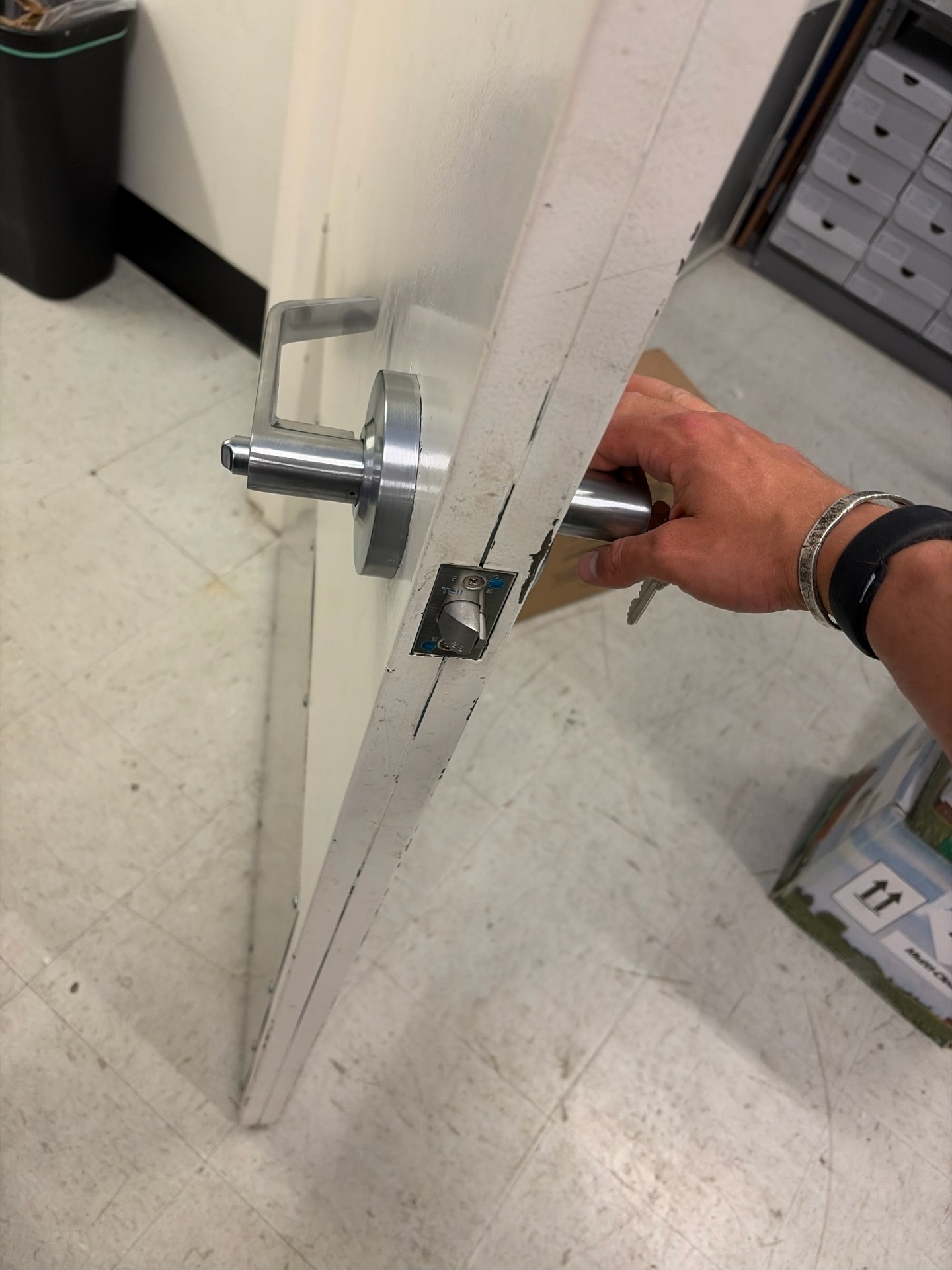 Commercial restroom door in Westminster with a metal keyed lever, keys at the cylinder, exposed latch, worn paint, and lower protective plate.