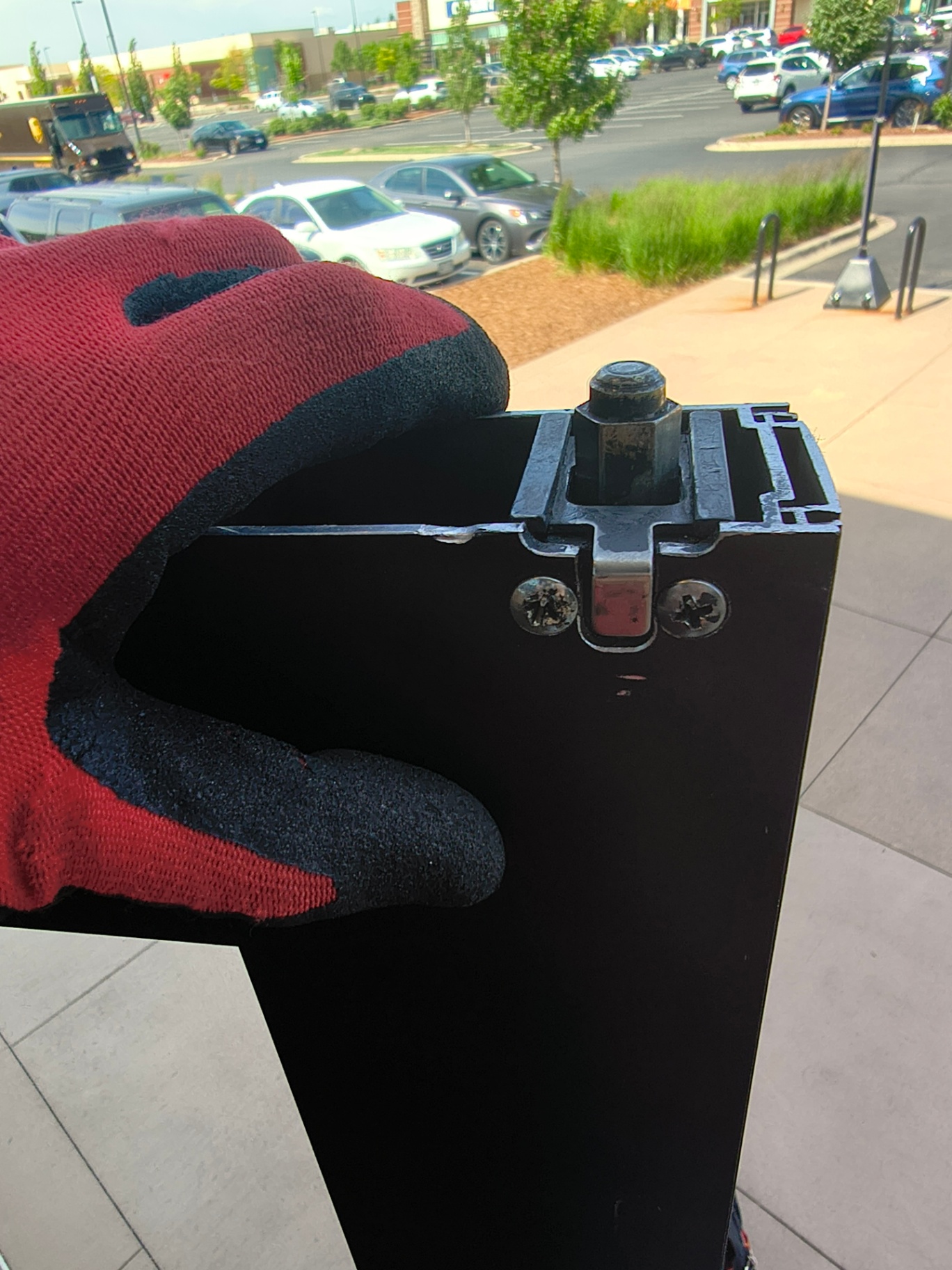 Gloved hand holding worn commercial exit-device hardware removed from a black-framed glass entrance in Westminster