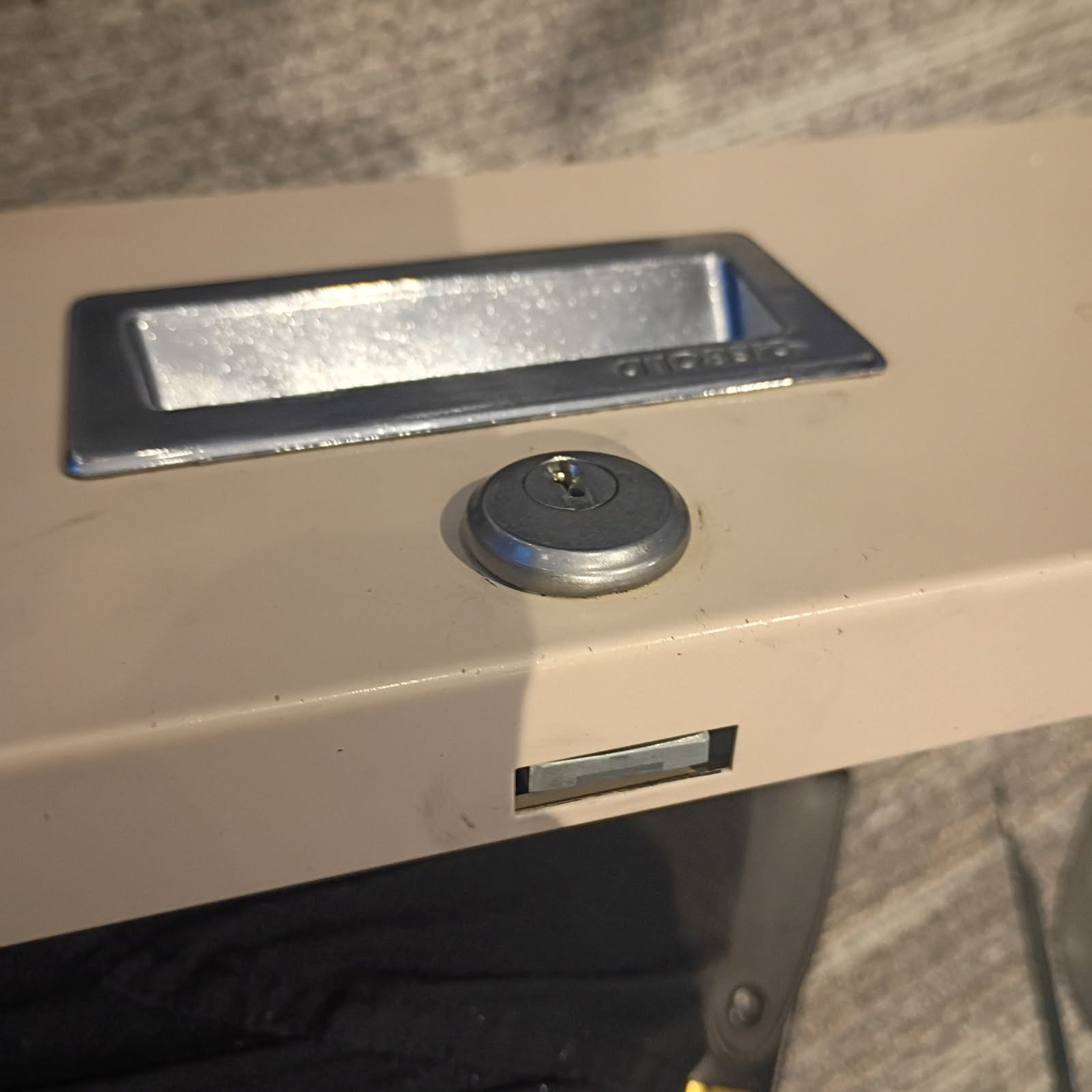 Close-up of a worn commercial cabinet or door with a chrome pull handle, round keyed cylinder, and exposed latch mechanism. - view 3