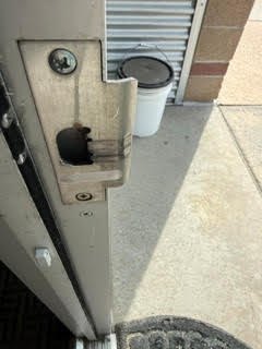 Close-up of exposed commercial door-edge latch hardware, lock cylinders, mounting marks, and an electronic-looking lock at a Lakewood business entrance.
