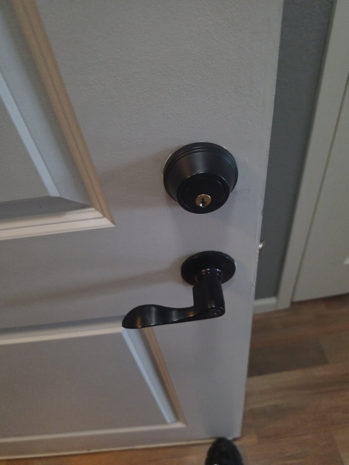 White paneled interior door in Littleton with a black deadbolt above a black lever handle, shown partially open.